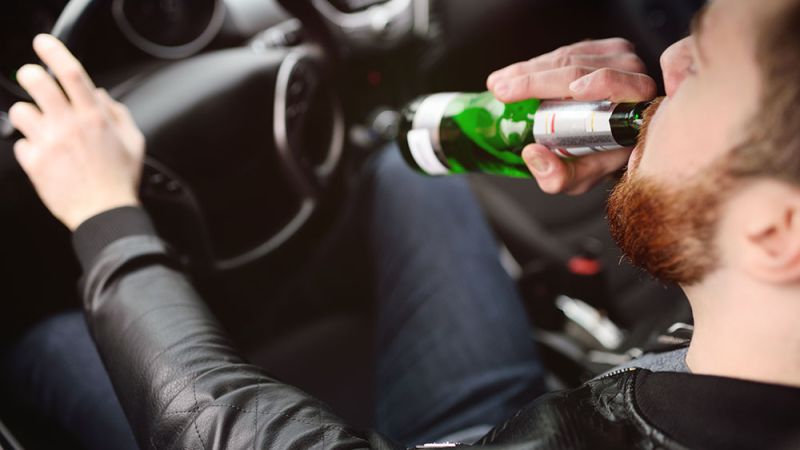 Driver drinking from a bottle while holding the steering wheel, illustrating dangers of distracted driving.