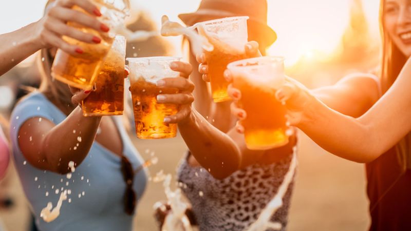Group of friends cheer with beer cups outdoors at sunset.