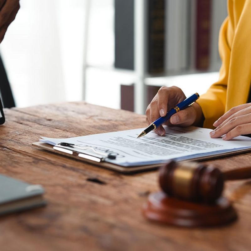 Person in yellow jacket signing document at desk with gavel and tablet, legal paperwork concept.