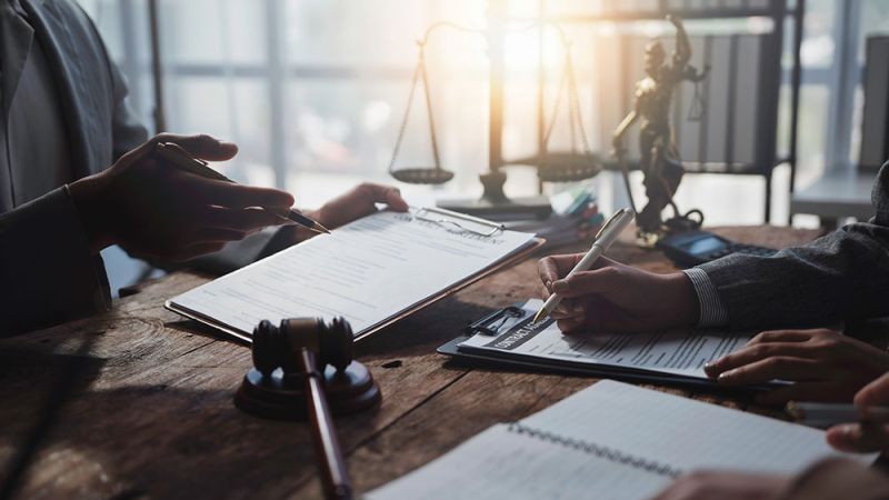 Lawyers reviewing legal documents at a desk with scales of justice in the background.