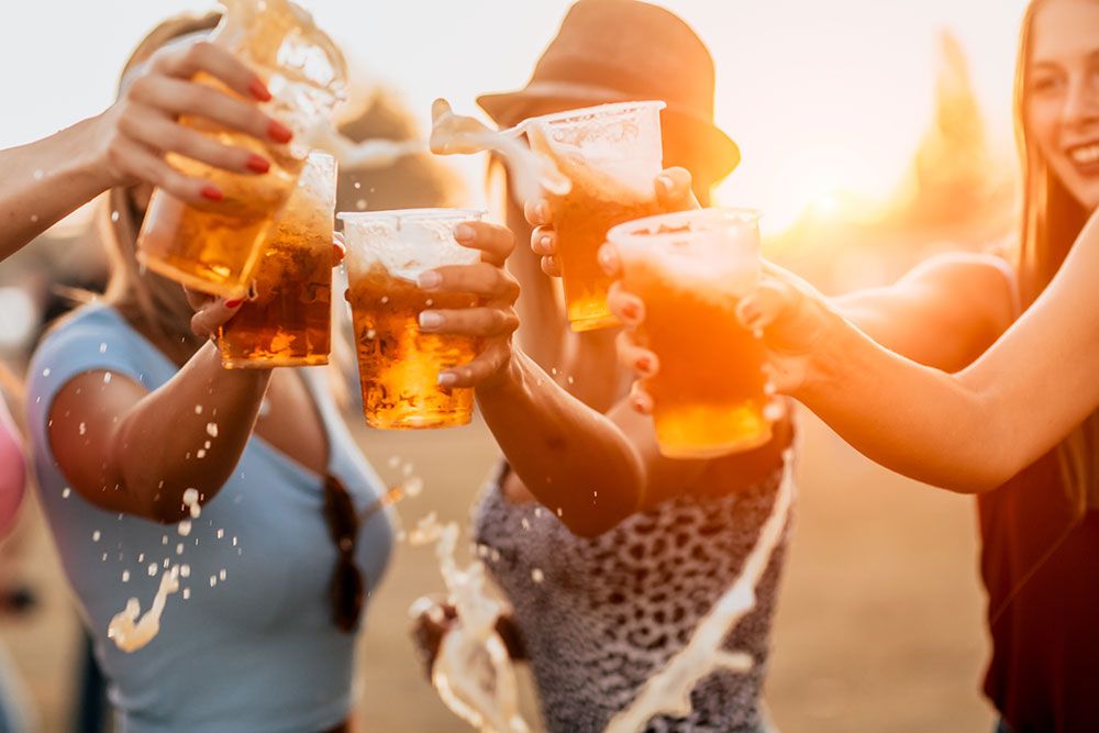 Group of friends cheer with beer cups outdoors at sunset.