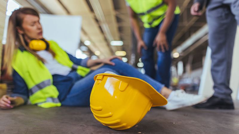 Construction worker injured on site, hard hat foreground, safety accident concept.