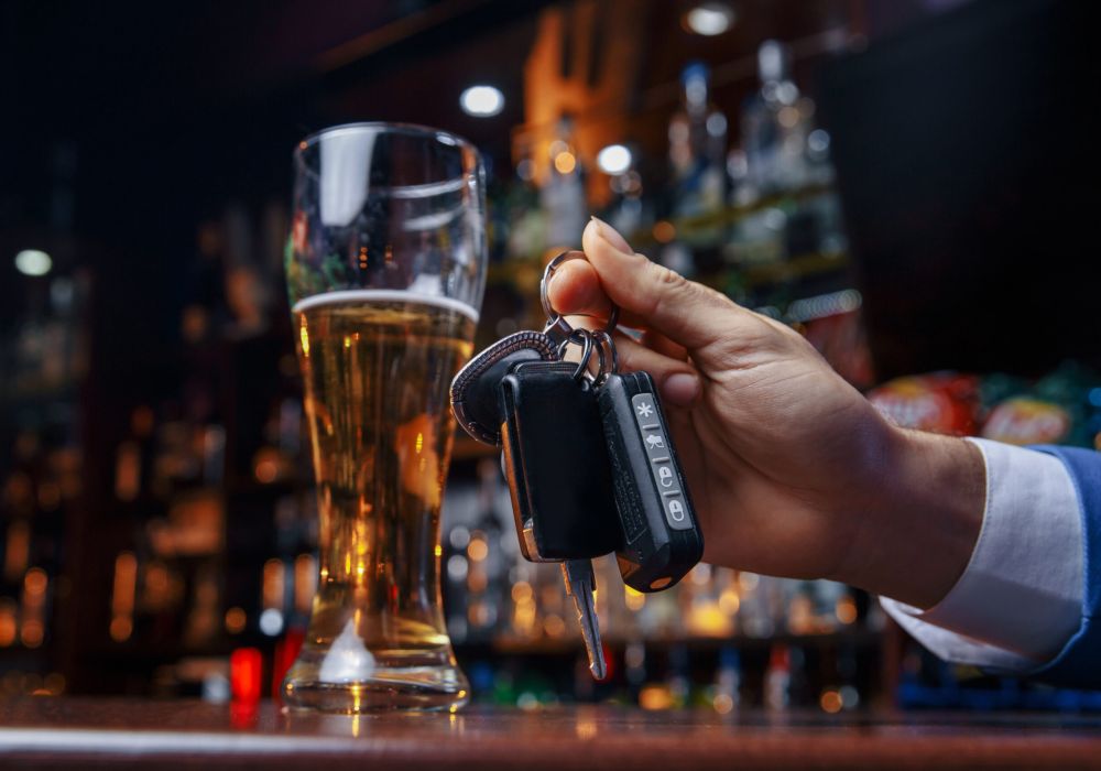 Hand holding car keys near a beer glass in a bar, highlighting responsible drinking and driving awareness.