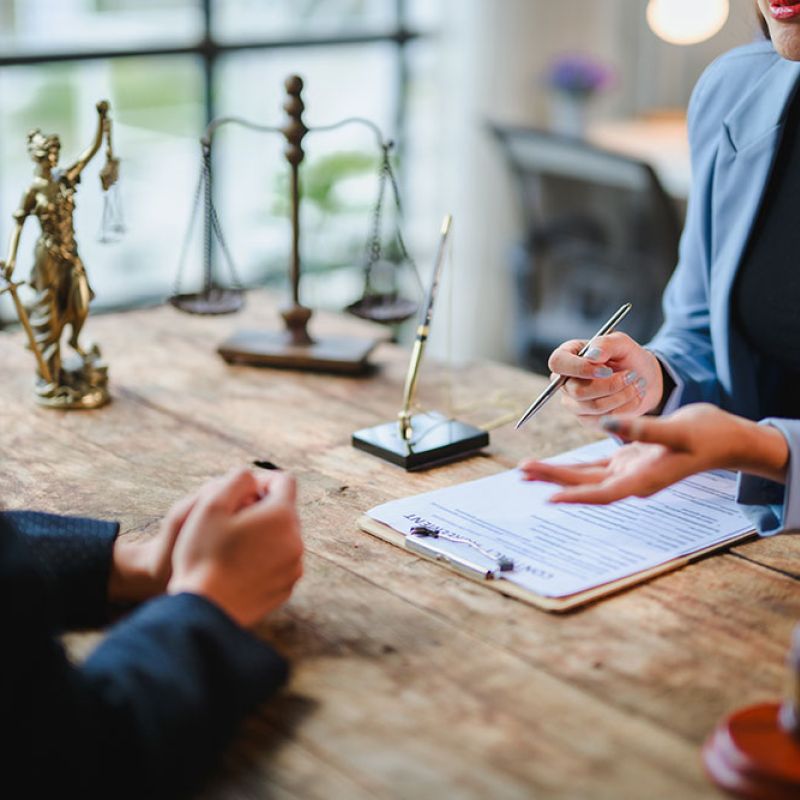 Two professionals discussing legal documents at a table with scales of justice and gavel in office setting.