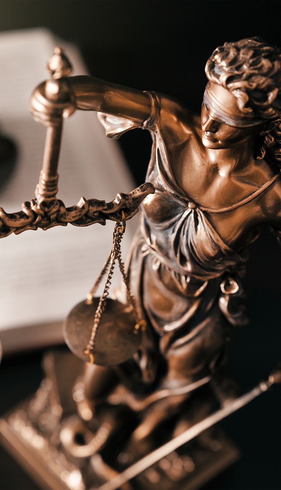 Bronze Lady Justice statue with scales and blindfold, symbolizing law and fairness, against an open book background.