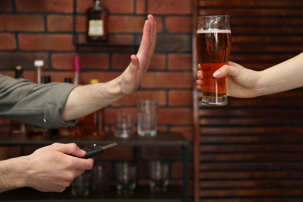 Person refusing a beer, holding car keys, promoting responsible driving.