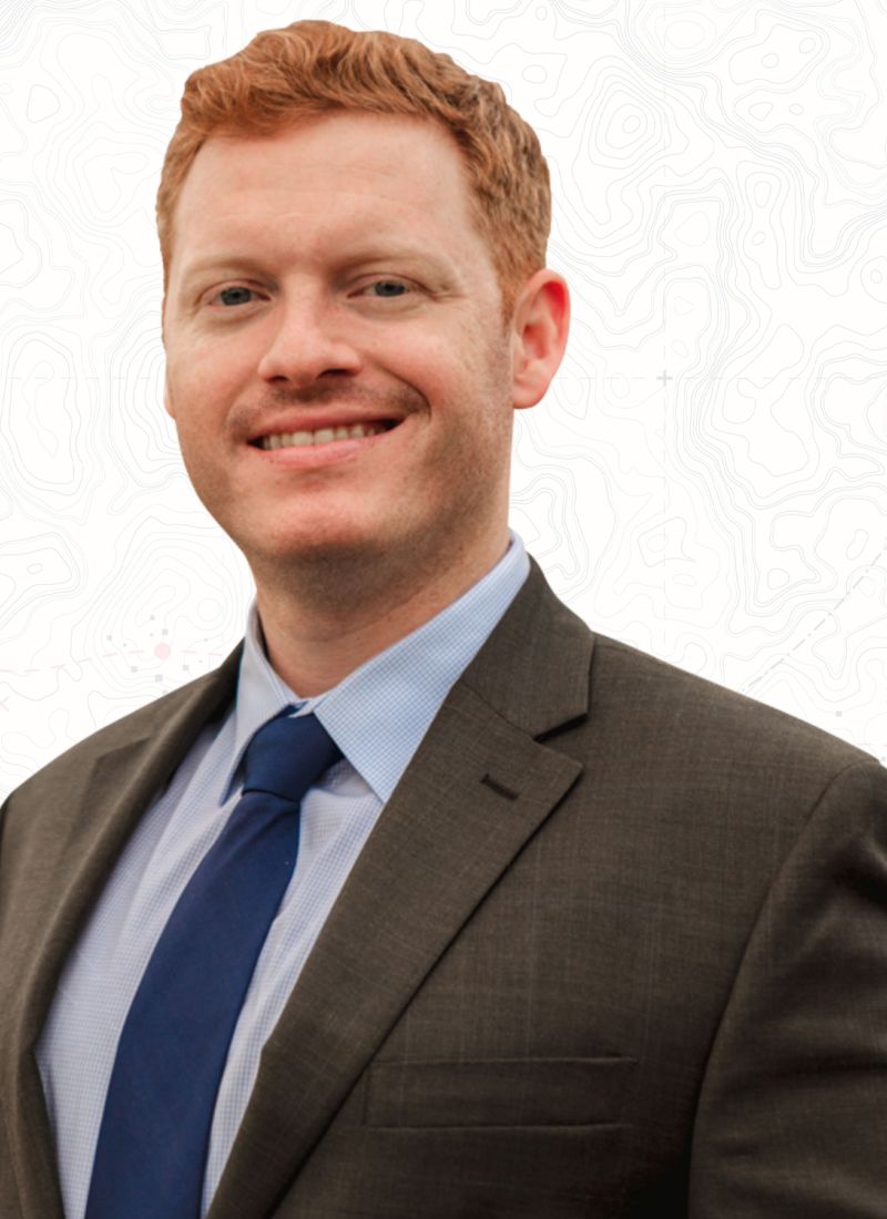 Smiling professional man in a suit and tie against a subtle topographic background.