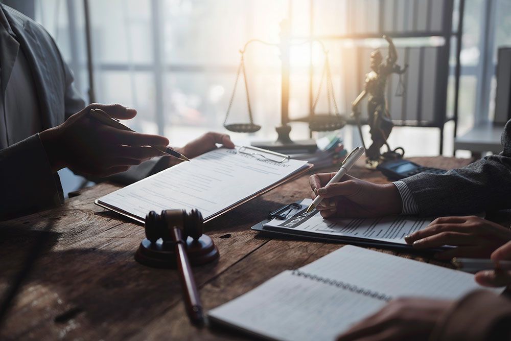 Lawyers reviewing legal documents at a desk with scales of justice in the background.