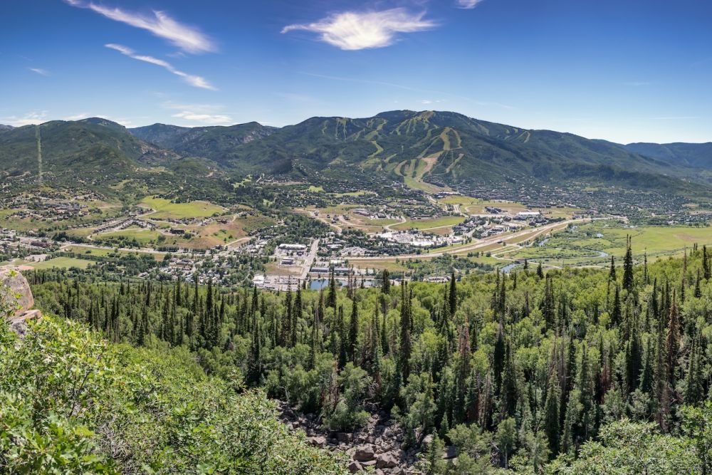 Panoramic view of mountain landscape with lush green forests and a quaint town nestled in a sunny valley below.
