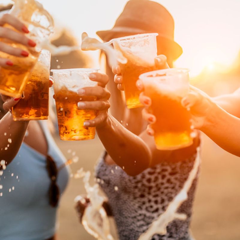Group of friends cheer with beer cups outdoors at sunset.