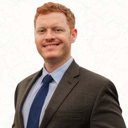 Smiling professional man in a suit and tie against a subtle topographic background.