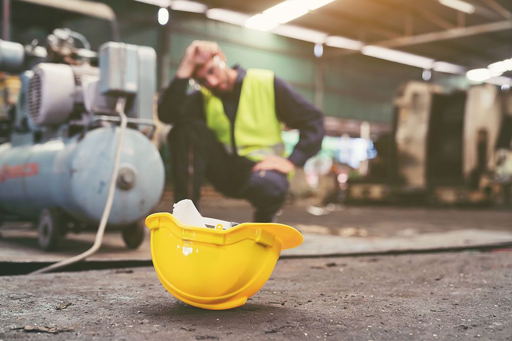 Worker in safety vest with yellow hard hat on the ground, focusing on safety at an industrial site.