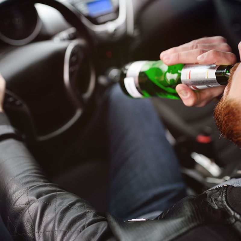 Driver drinking from a bottle while holding the steering wheel, illustrating dangers of distracted driving.