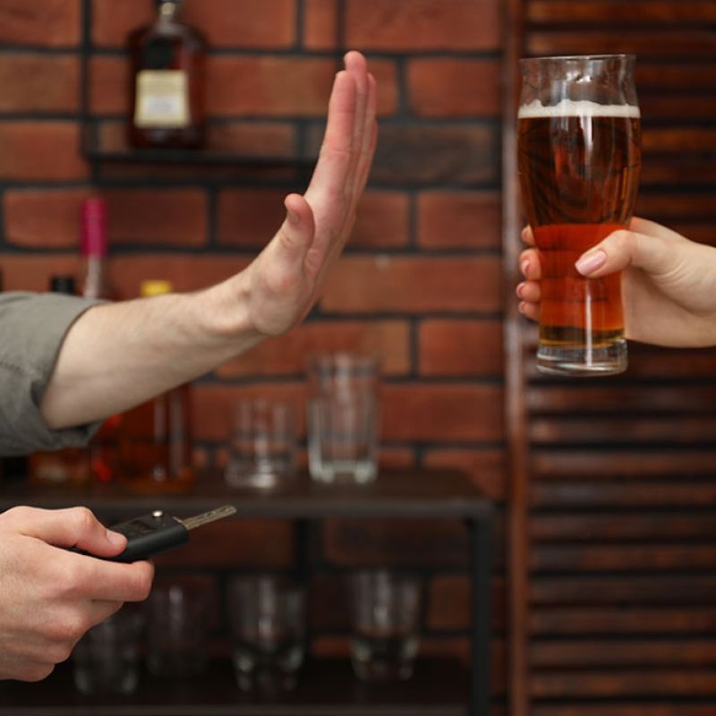 Person refusing a beer, holding car keys, promoting responsible driving.
