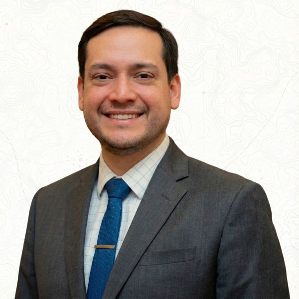 Ryan Reyna in a suit and tie with a white patterned background.