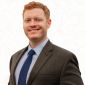 Smiling professional man in a suit and tie against a subtle topographic background.