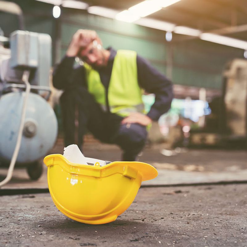 Worker in safety vest with yellow hard hat on the ground, focusing on safety at an industrial site.