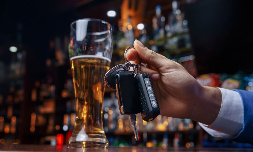 Hand holding car keys near a glass of beer at a bar, emphasizing responsible drinking and driving awareness.