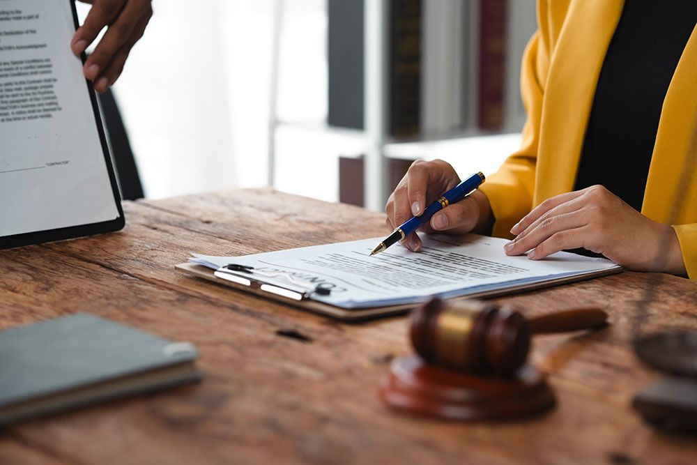 Person in yellow jacket signing document at desk with gavel and tablet, legal paperwork concept.