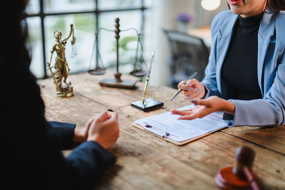 Two professionals discussing legal documents at a table with scales of justice and gavel in office setting.