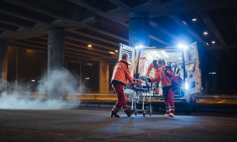 Emergency medical team loading a patient into an ambulance under a bridge at night.