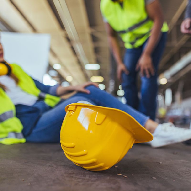 Construction worker injured on site, hard hat foreground, safety accident concept.