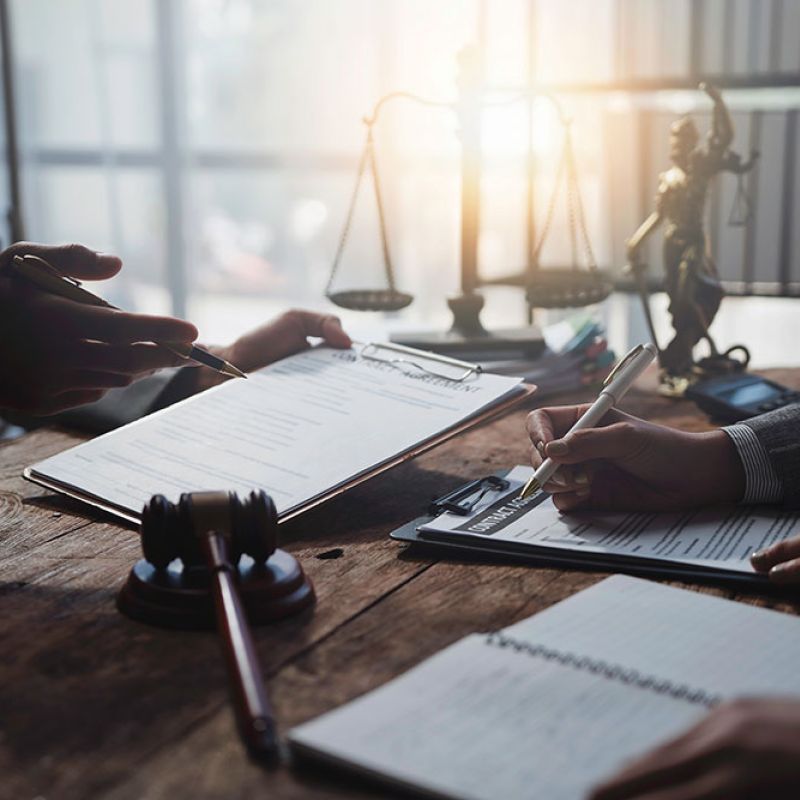 Lawyers reviewing legal documents at a desk with scales of justice in the background.
