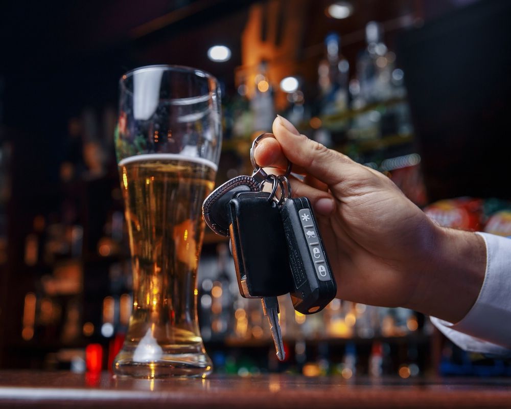 Hand holding car keys near a glass of beer at a bar, emphasizing responsible drinking and driving awareness.