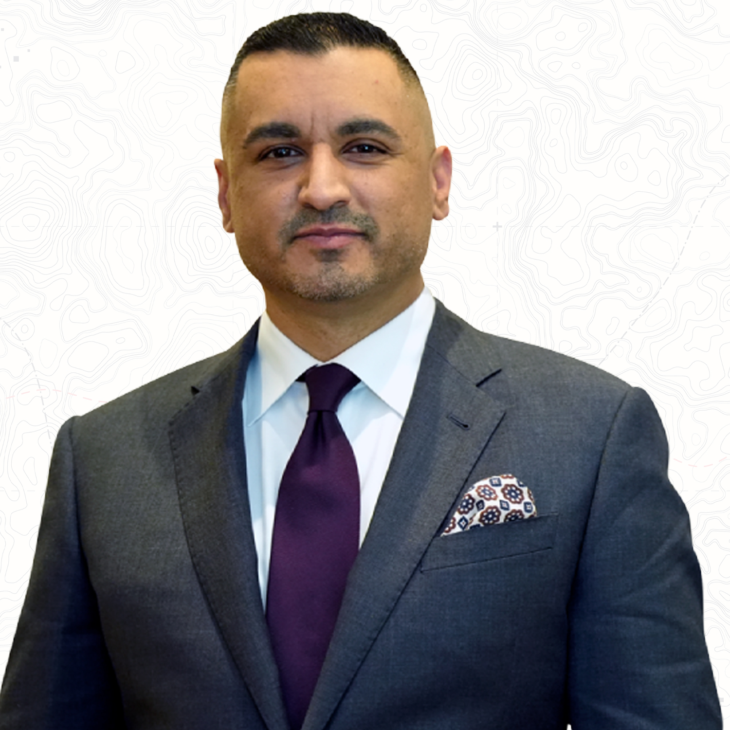 Business professional in a suit and tie, standing against a white background with a subtle pattern.