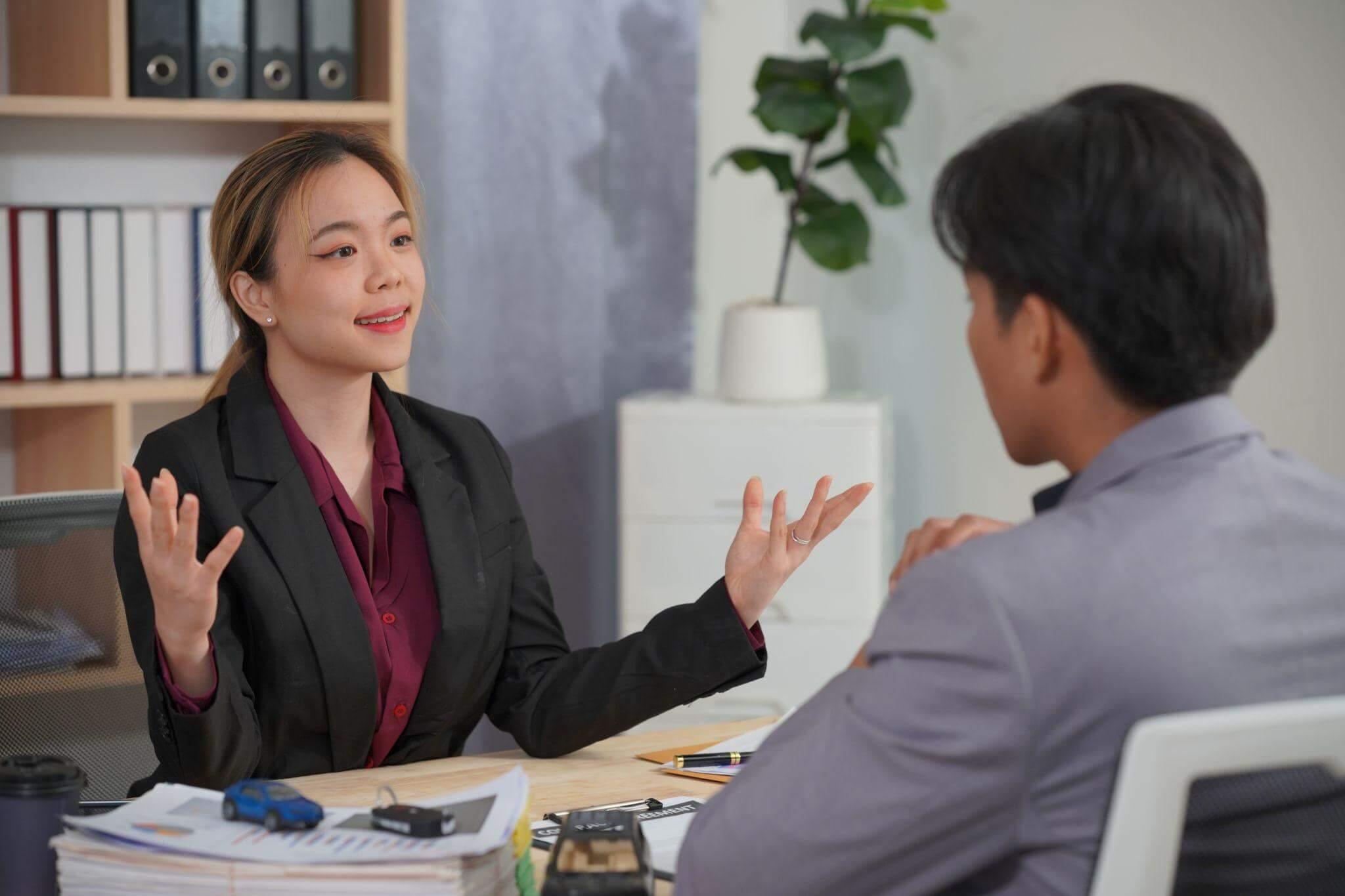 a woman sitting at a desk talking to a man