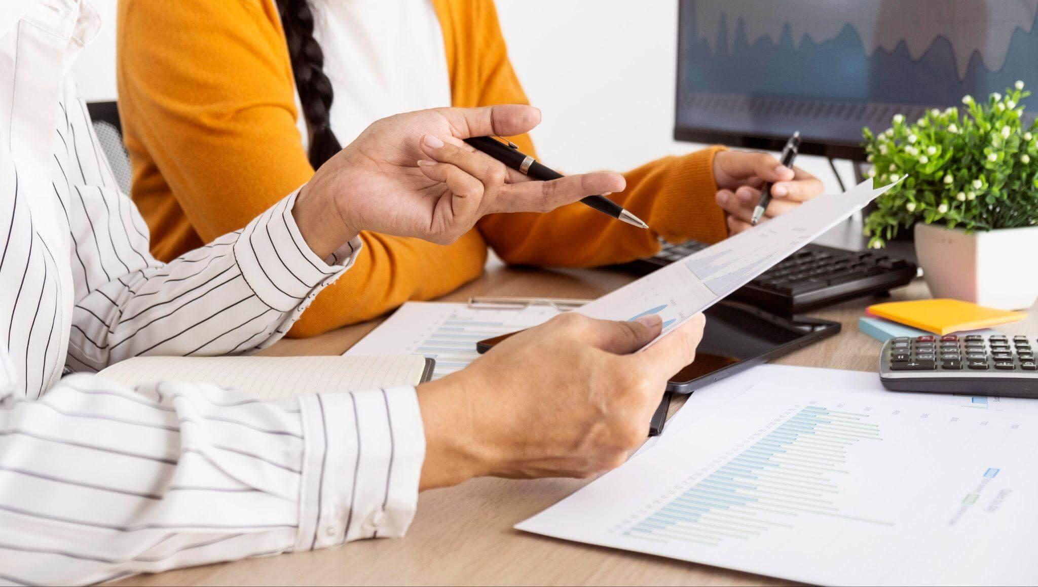 two people sitting at a desk with papers and a calculator