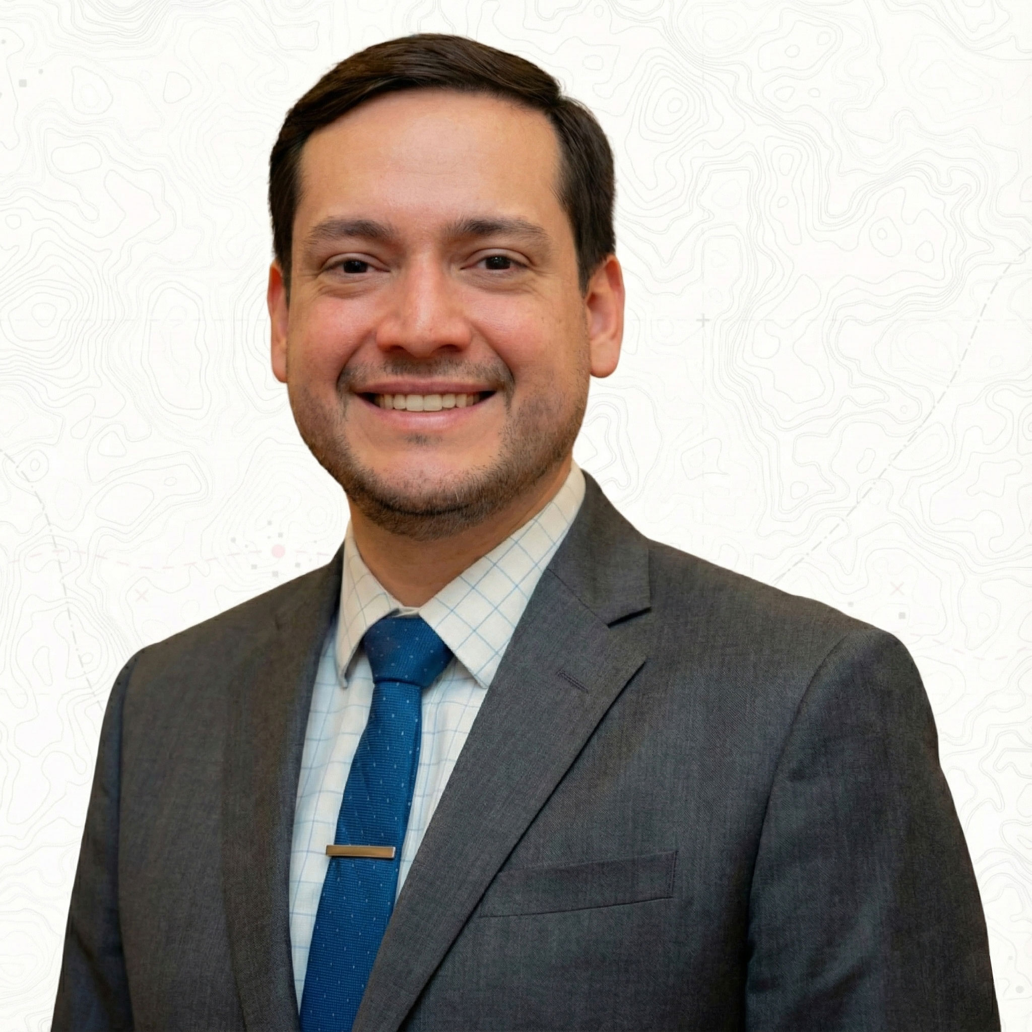Ryan Reyna in a suit and tie with a white patterned background.